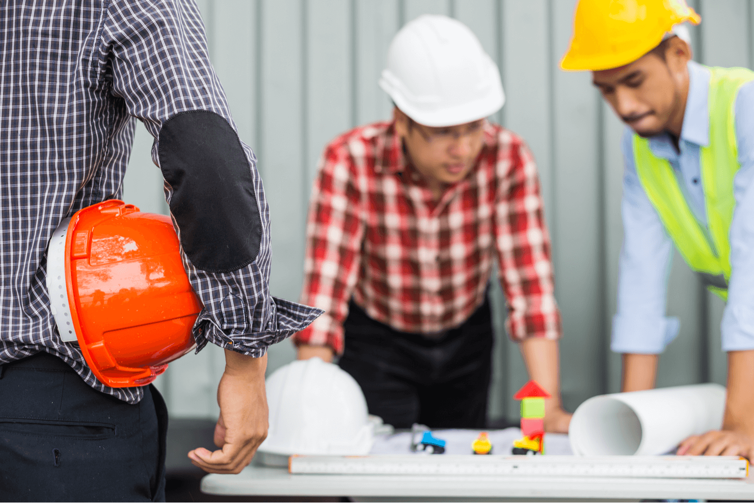 Man holding hardhat watching others go over plans